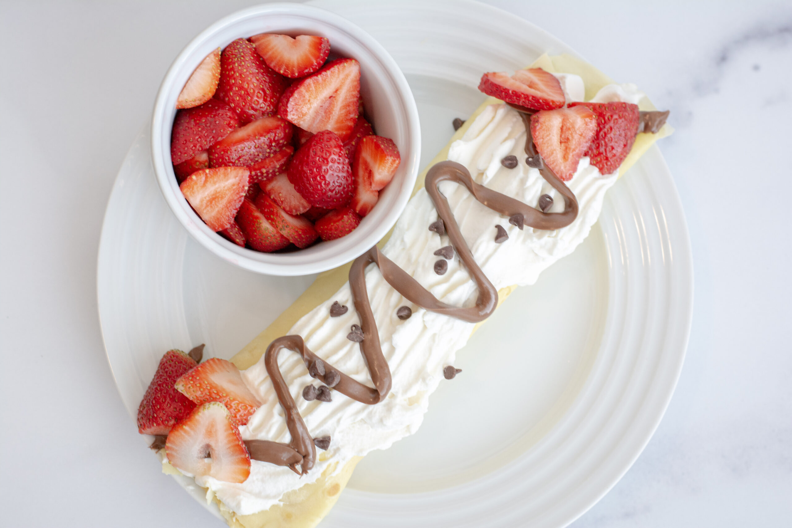 One single crepe on a plate topped with strawberries and whipped cream.