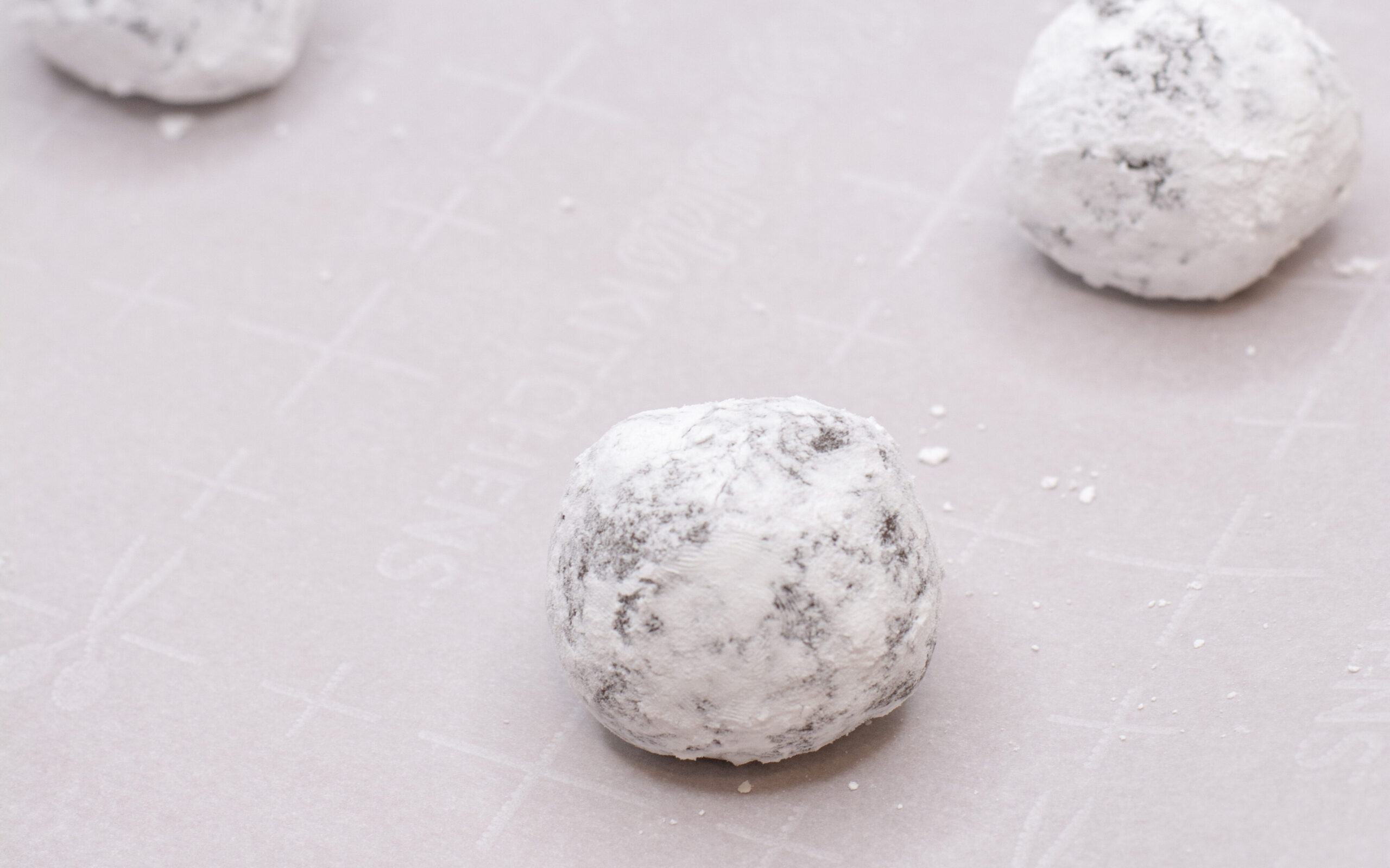 Cookie dough ball of chocolate crinkle cookies covered in powdered sugar on a pan.