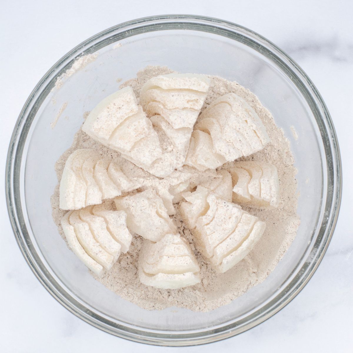 Onion in a bed of flour and spices in a bowl.