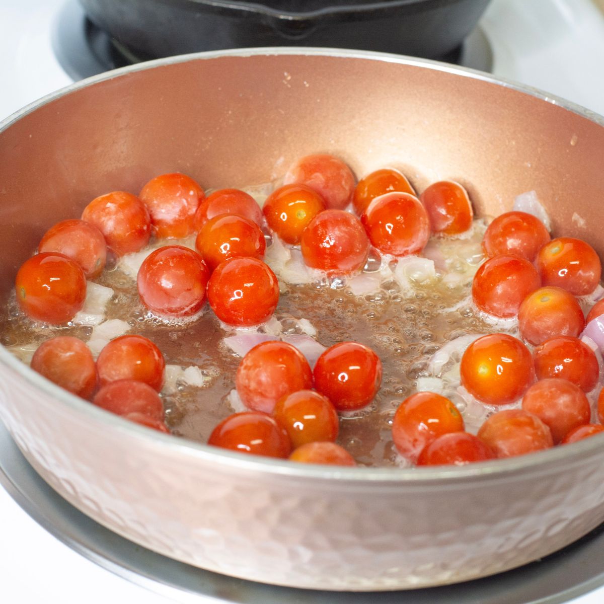 Cherry tomatoes in a frying pan with shallots. 