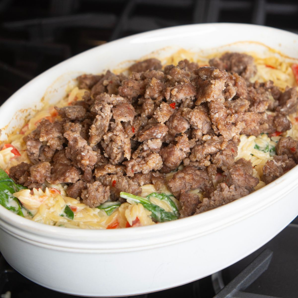 large casserole dish with orzo, sausage, spinach, red peppers and cheese.