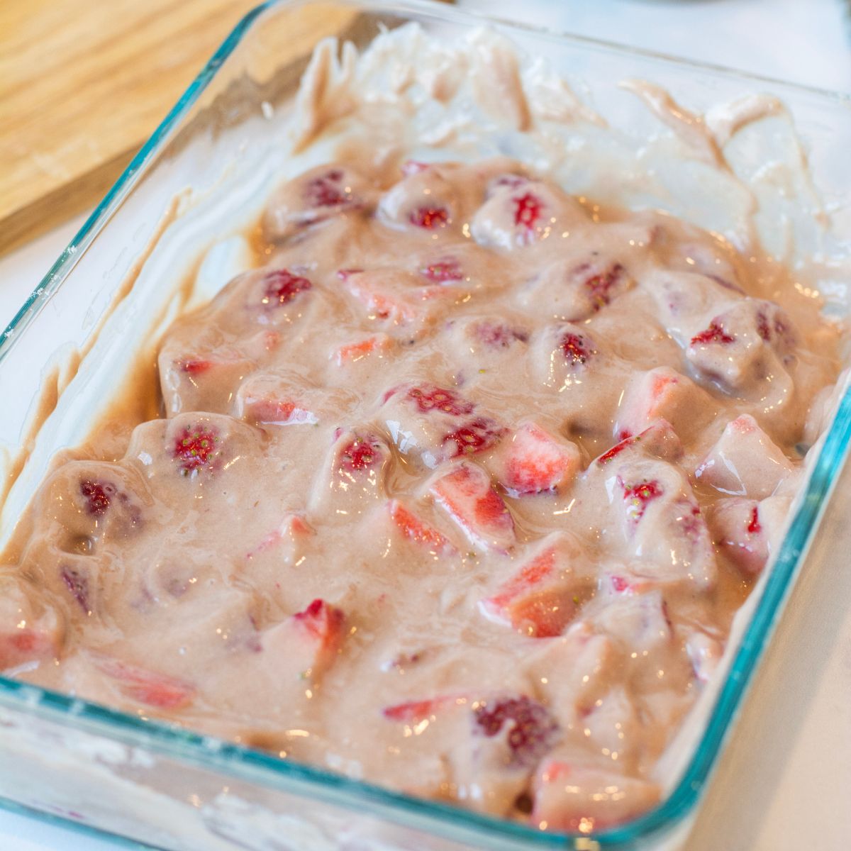 Strawberry chunks mixed into a container filled with greek yogurt, protein powder and other ingredients.