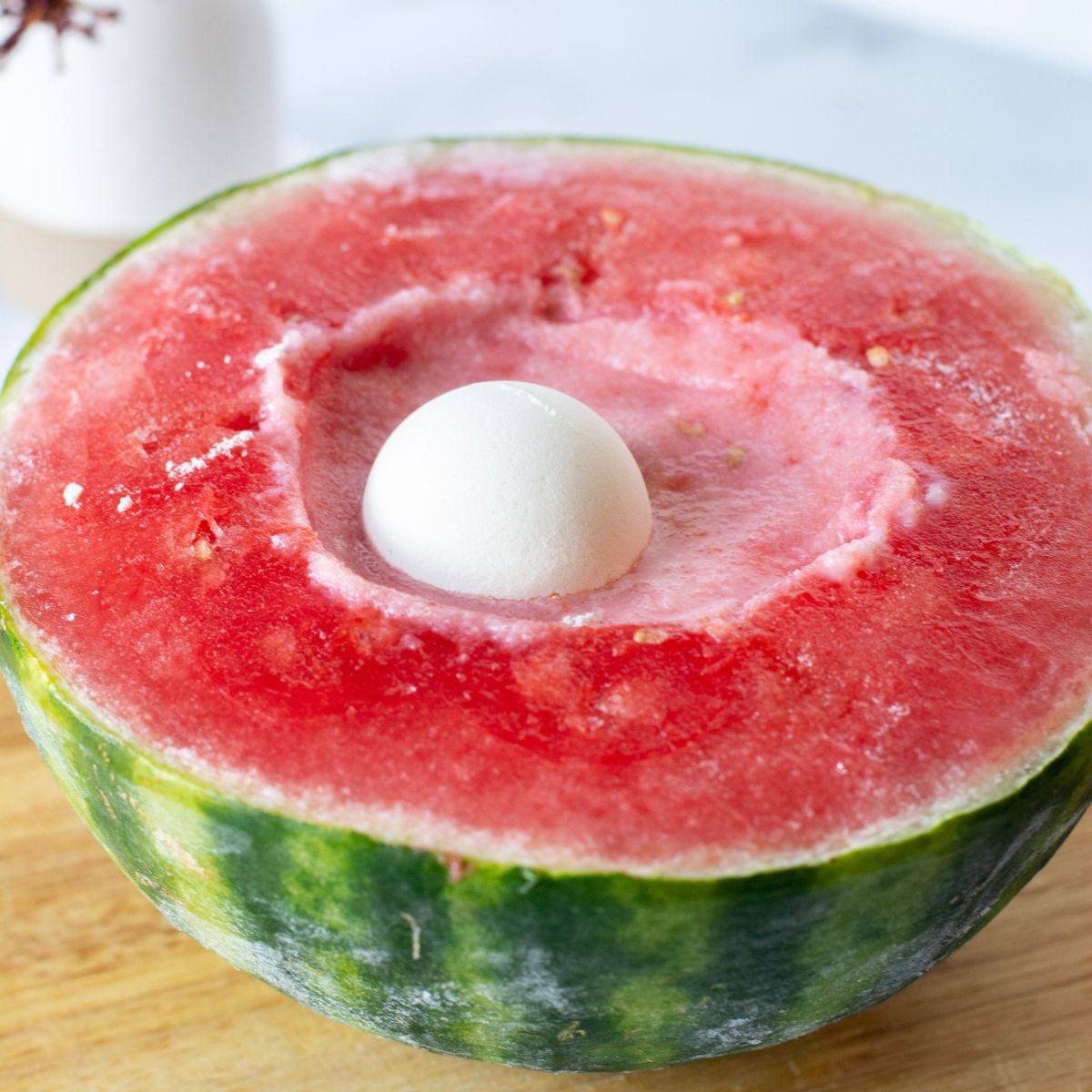 Watermelon half with protein powder scoop and cream in the well of the watermelon.