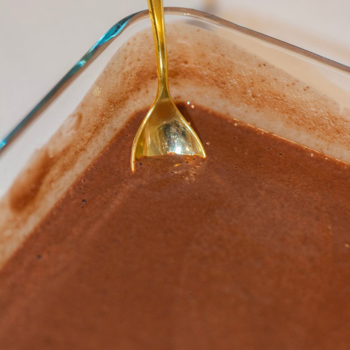 Chocolate Protein Chia pudding in a glass container with a golden spoon.