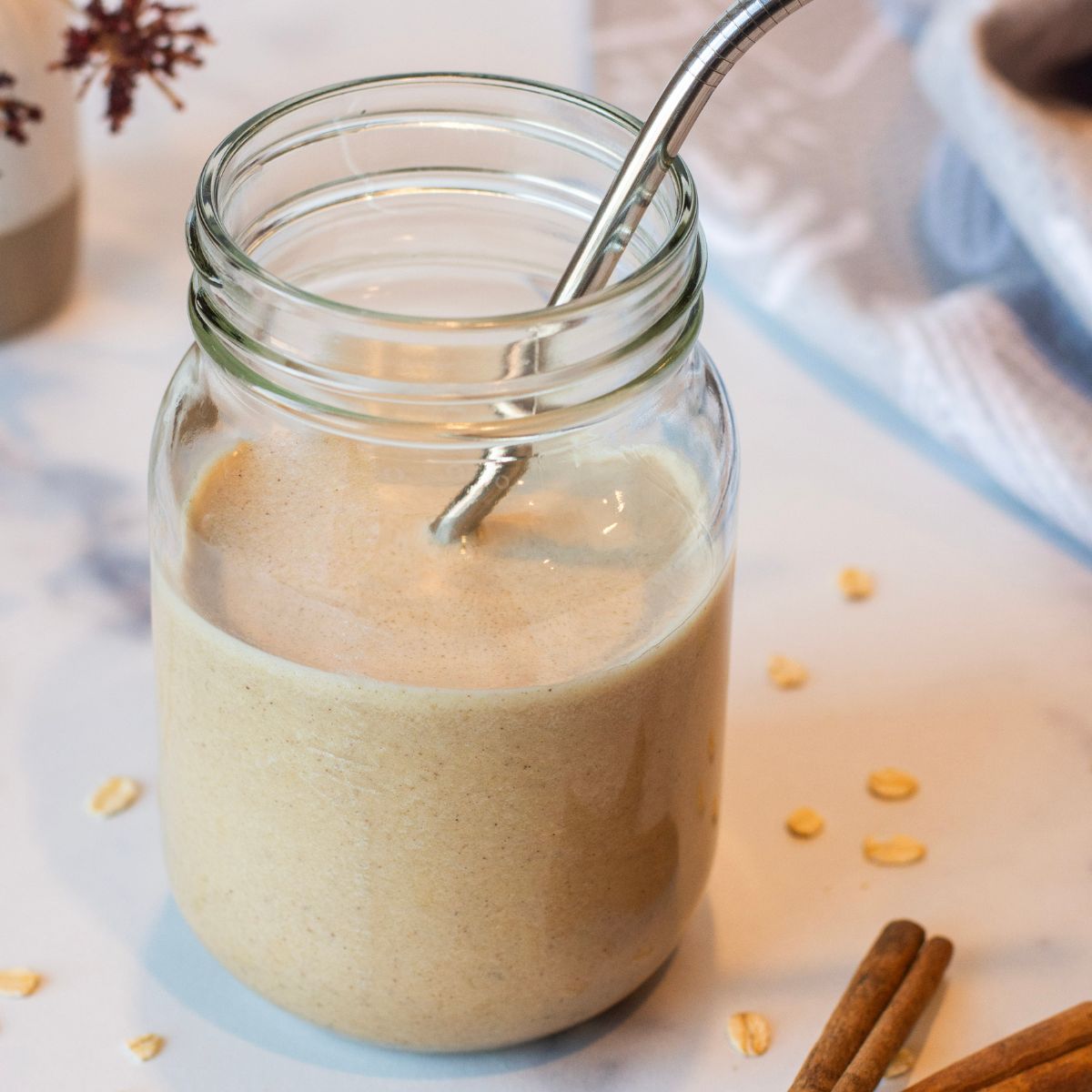 Smoothie poured into a mason jar placed on the countertop with a metal straw and cinnamon and oats sprinkled on top.