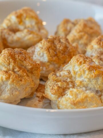 High-Protein fluffy cinnamon bites on a plate sprinkled with cinnamon and syrup.