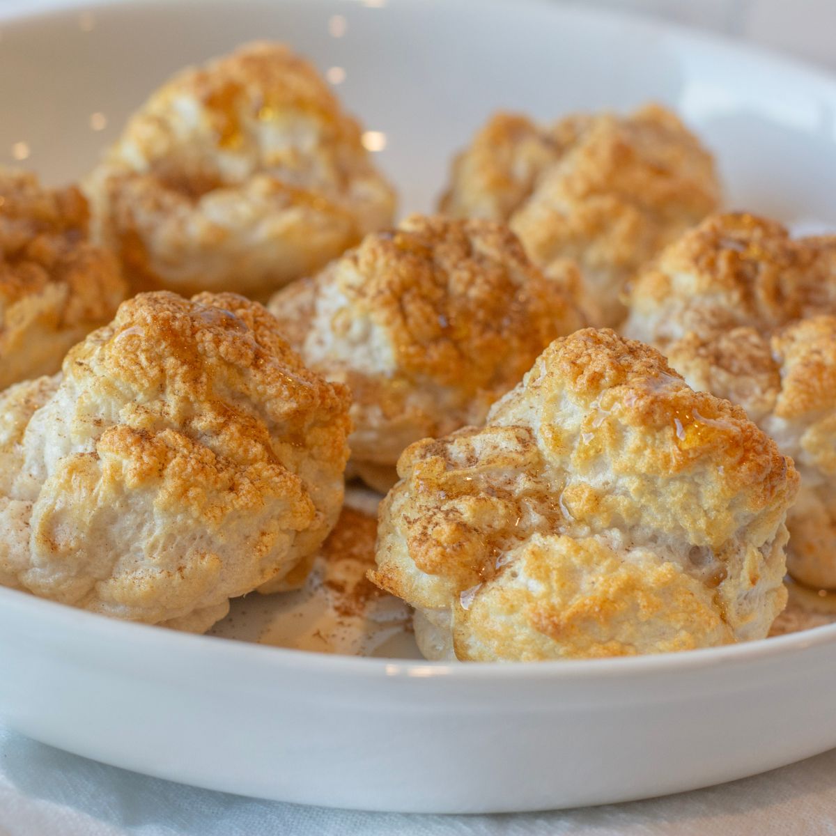 maple syrup and cinnamon sugar sprinkled over the top of a bowl of fluffy cinnamon bites