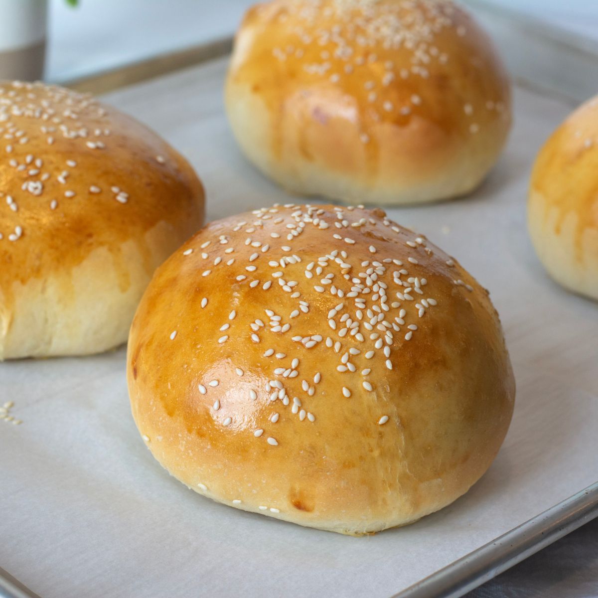 Homemade hamburger buns on a sheet pan topped with sesame seeds.