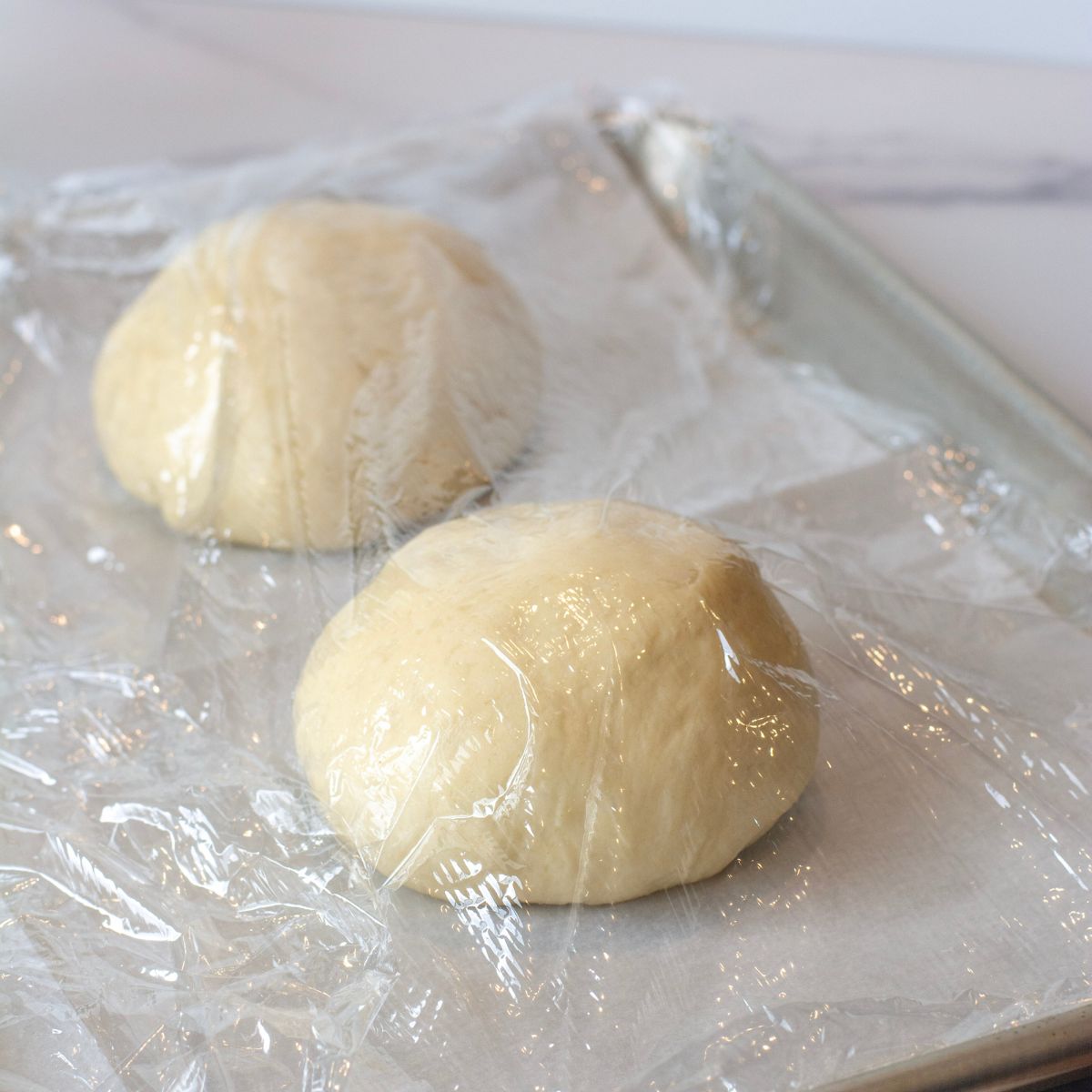 Buns placed on a baking sheet in dough balls for a second rise.