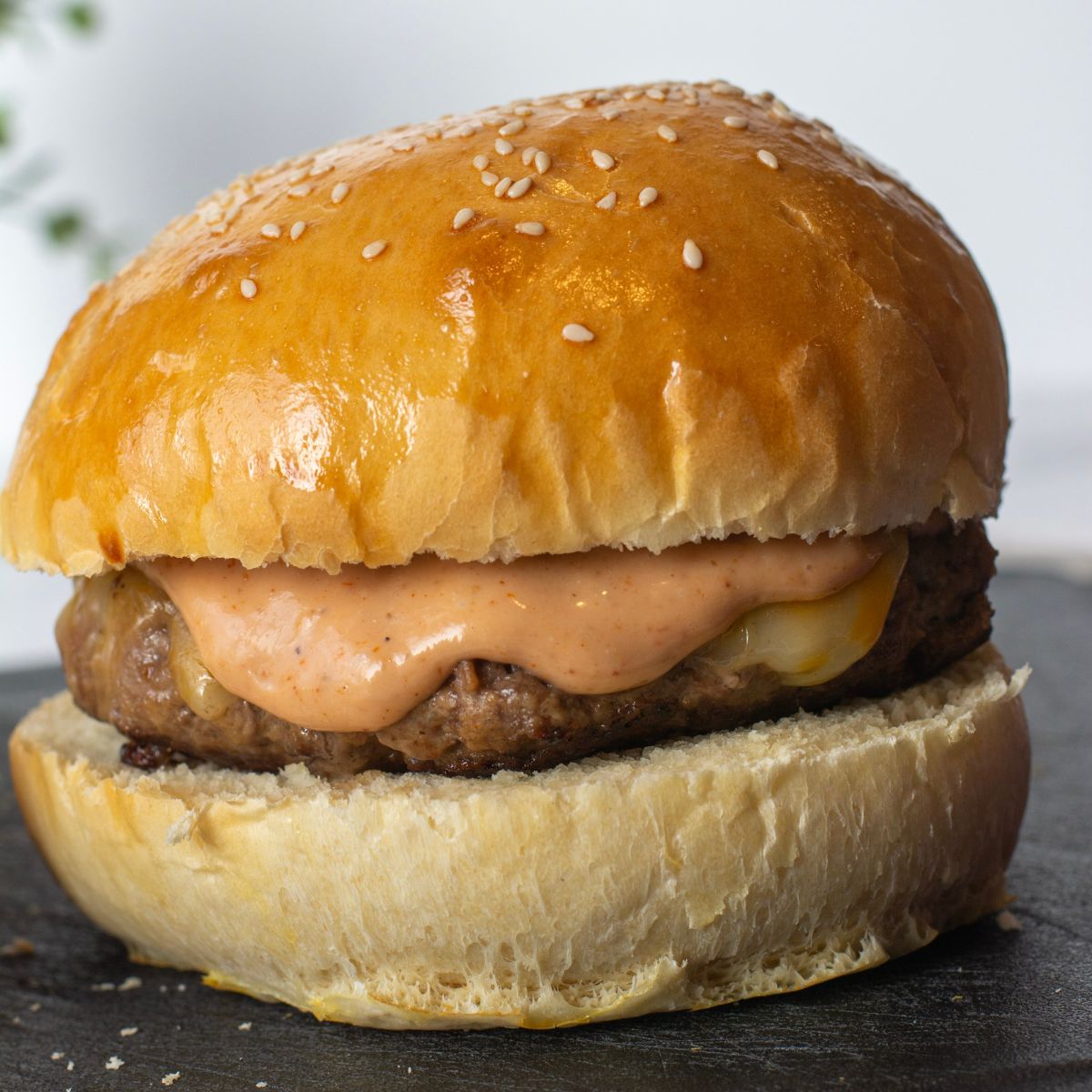 Hamburger buns stacked to form a hamburger with a beef patty and melted cheese and sauce dripping off the entire burger.