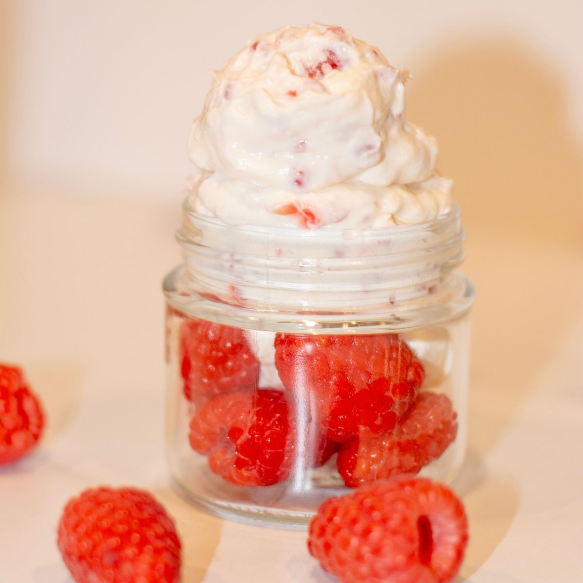 A bowl of raspberry cheesecake protein jello in a bowl with lots of raspberries on the table around it.